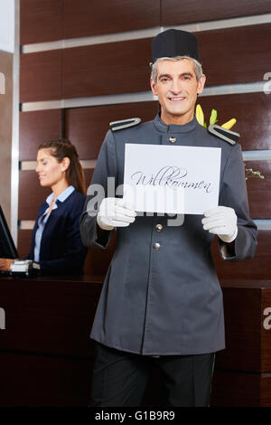 Lächelnd Hotel Concierge halten Schild mit der Aufschrift in Deutsch "Willkommen" (willkommen) Stockfoto