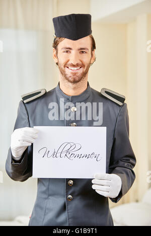 Lächelnd Hotelseite halten deutsche Schild mit der Aufschrift "Willkommen" (willkommen) Stockfoto