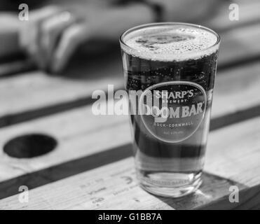 Ein Pint von bekanntem Bier, das man im Sommer auf einer Holzbank in einem Biergarten sieht. Stockfoto