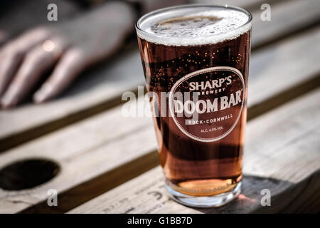 Ein Pint von bekanntem Bier, das man im Sommer auf einer Holzbank in einem Biergarten sieht. Stockfoto