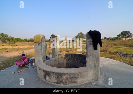 Einen tiefen Brunnen in Khajuraho Dorf mit einer ländlichen Frau waschen mit Javari-Tempel im fernen Hintergrund, Madhya Pradesh, Indien Stockfoto