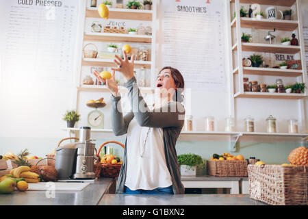 Junge Frau mit Zitrone Saft Bar jongliert. Glückliche junge Arbeitnehmerin spielen mit Früchten an Saftbar. Stockfoto