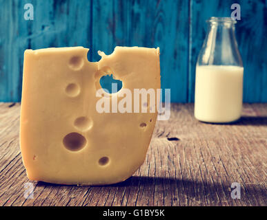 Nahaufnahme von einem Stück Schweizer Käse und eine Glasflasche mit Milch auf einem rustikalen Holztisch, gegen einen blauen rustikalen hölzernen Zeitmessung Stockfoto