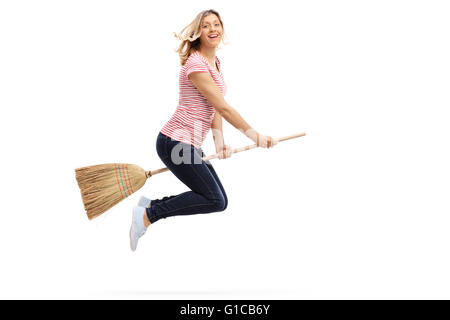 Fröhliche junge Frau auf einem Besen fliegen und schaut in die Kamera, die isoliert auf weißem Hintergrund Stockfoto