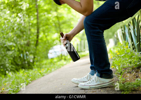 Mann mit Bierflasche auf grünen Zaun im Freien sitzen deprimiert. Stockfoto