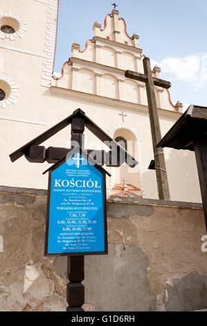 Informative Kirche Kreuz in Janowiec Dorf, Polen, Europa, blaue Brett mit Masse Zeitplaninformationen vor Gebäude. Stockfoto