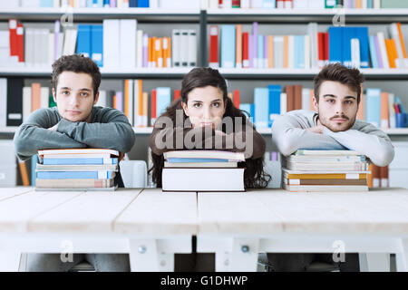 Junge College-Studenten in der Bibliothek gemeinsam studieren, sie stützte sich auf einen Stapel Bücher und Blick in die Kamera Stockfoto