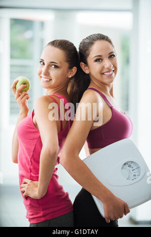 Sie sind glücklich Teenager Freundinnen hält einen Apfel und eine Skala, posiert und lächelnd in die Kamera, Fitness und Gewicht-Verlust-Konzept Stockfoto