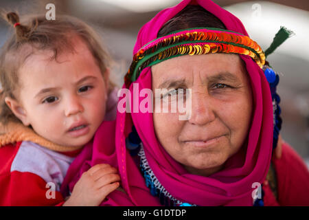 Mutter trägt ihr Baby im lokalen Kopfkleid auf dem Rücken in der Landschaft der Provinz Aydin, Türkei.