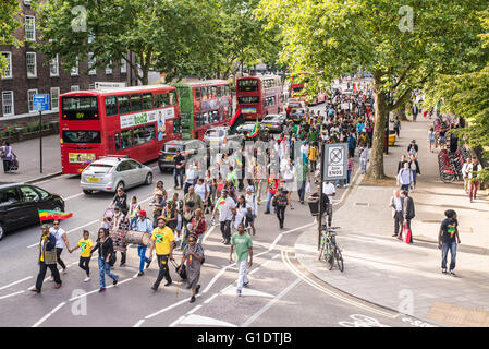 Straße Demonstration mit afro-karibischen Menschen in einer belebten Straße in London marschierend, mit Fahnen und Trommeln. Stockfoto