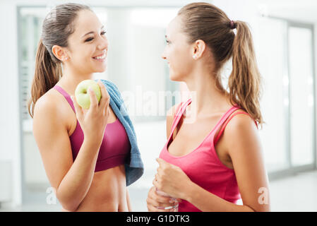 Schöne Mädchen in der Turnhalle genießen und miteinander reden, während einer Pause Training, hält man einen Apfel, Fitness und gesunde li Stockfoto