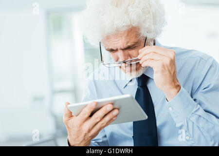 Unternehmer haben Sehprobleme, er nutzt eine Tablette und Anpassung seiner Brille, Büroeinrichtung auf Hintergrund Stockfoto