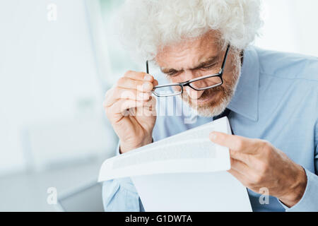Reifen männlichen Büroangestellten haben Sehprobleme beim Papierkram mit kleinem Text lesen Stockfoto