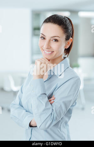 Selbstbewusste Frau posiert mit Hand am Kinn und lächelt in die Kamera Stockfoto