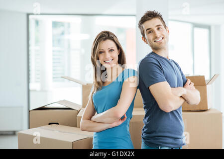 Lächelnd Liebespaar posiert in ihrem neuen Haus, Rücken an Rücken umgeben von Kartons Stockfoto