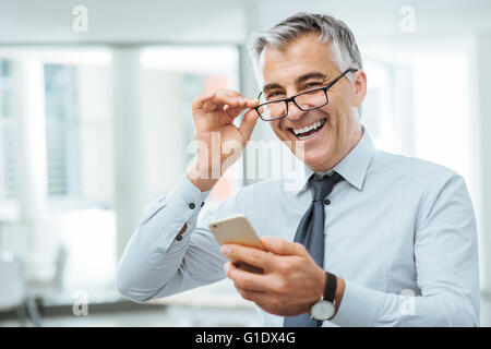 Lächelnd Geschäftsmann mit Sehprobleme, wird er seine Brille anpassen und etwas auf seinem Handy zu lesen Stockfoto