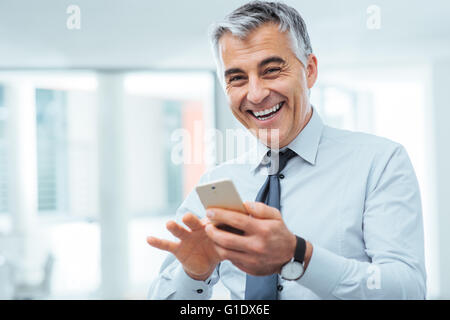 Fröhliche Geschäftsmann mit einem Touch Screen Smartphone und Blick in die Kamera Lächeln Stockfoto