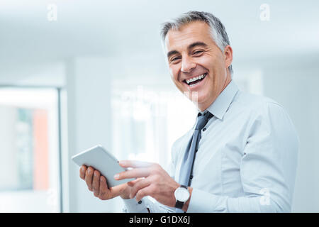 Lächelt zuversichtlich Geschäftsmann Blick in die Kamera und mit einem digital Touch-Screen-Tablette Stockfoto