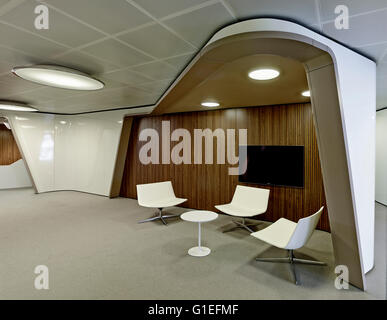 Inaugure Büros, Barcelona, Spanien. Arbeitsbereich mit weißen modernen Stühlen unter einer Kurve in der Decke. Holz Verkleidung an Wand mit einem flachen Fernseher mit Flachbildschirm. Stockfoto