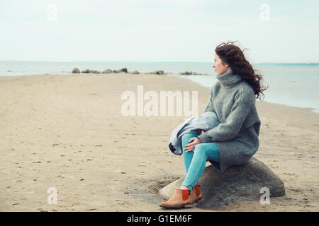 Attraktive Frau trägt eine warme Strickjacke am kalten Strand Stockfoto