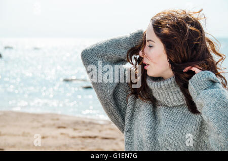 Attraktive Frau trägt eine warme Strickjacke am kalten Strand Stockfoto