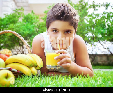 Portrait eines glücklich Teen jungen auf frischen grünen Wiese liegend und trinken lecker Saft, Obst zu essen Stockfoto