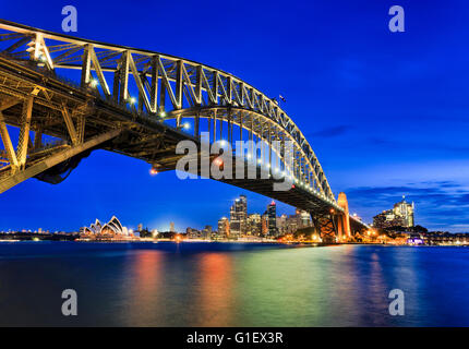 Seitenansicht der Sydney Harbour Bridge in Richtung Stadt CBD, die Felsen und Circular Quay bei Sonnenuntergang über den unscharfen reflektierenden harbour Stockfoto