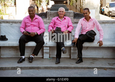 Drei kubanische Sänger gekleidet in rosa Hemden und Cowboyhüte sitzen auf einer Bank in Havanna Centro Kuba Stockfoto