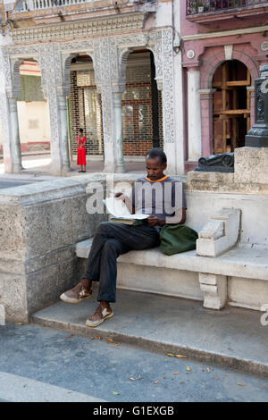Ein kubanische Mann sitzt auf den Stein sitzen auf dem Prado in Centro Havanna Kuba mit klassischen Säulen Architektur hinter lesen Stockfoto