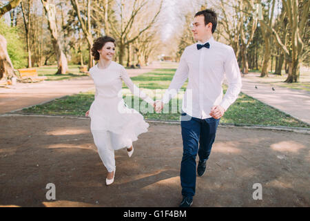 Glückliches Hochzeitspaar charmant Bräutigam und die Blonde Braut läuft mit verbundenen Händen an der Stadt Park road Stockfoto