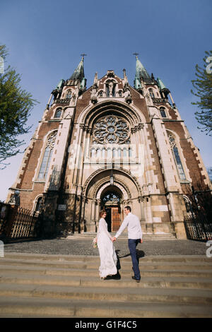 Schöne Braut bei der Hochzeit Kleid Vorbereitung auf die Zeremonie in der Kirche. Zu Fuß zurück halten die Hände in der Nähe von alte Burg Stockfoto