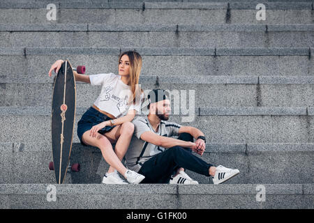 Stilvolle junges Paar auf Betontreppen mit einem longboard Stockfoto