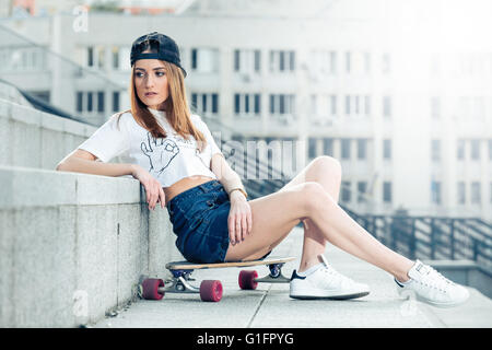 Junge Frau sitzt auf Longboard in der urbanen Landschaft Stockfoto