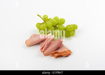 Scheiben vom Schinken und weiße Weintraube auf weißem Hintergrund Stockfoto