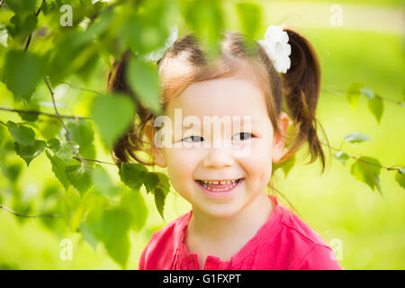 Nahaufnahme des Gesichtes des Kindes spielen verstecken und suchen im Freien im Park. Wunderschönes kleines Mädchen versteckt sich hinter riesigen Baum im Sommer Stockfoto