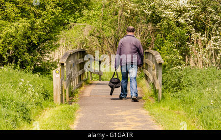 Ein Mann geht über eine Holzbrücke, wie er auf einem öffentlichen Wanderweg geht entlang dem Fluss Kennet in Reading, UK Stockfoto