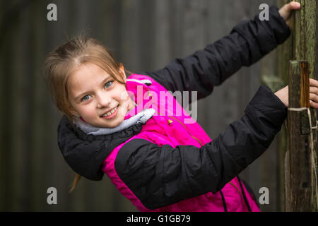 Fröhliches kleines Mädchen Portrait am Zaun im Dorf. Stockfoto