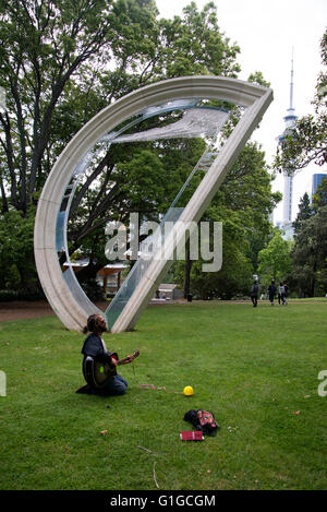 Bärtiger junger Mann in Gläsern kniet auf dem Rasen seine Gitarre im Albert Park zu spielen. Stockfoto