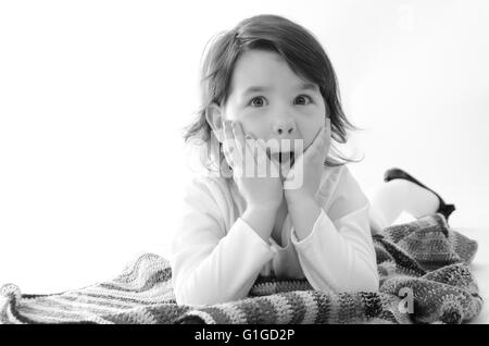 Süßes Mädchen erstaunt Sit auf farbige Decke isoliert auf weiss Stockfoto