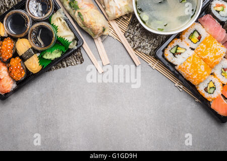 Sushi-Menü mit Sommer rollt in Reispapier Verpackungen und Miso-Suppe auf grauem Stein Hintergrund, Draufsicht, Grenze.  Japanisches Essen Stockfoto