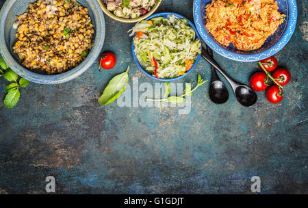 Gesunde vegetarische Salate in rustikale Schalen mit Löffel auf Vintage-Hintergrund, Draufsicht, Platz für Text, Grenze.  Healt Stockfoto