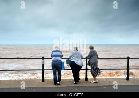 Mann und zwei Frauen Blick auf das Meer an einem stürmischen Tag In Sidmouth UK Stockfoto