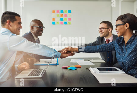Gemischtrassig Geschäftsteam signalisieren ihre Verpflichtung, einander durch das erreichen über den Tisch im Büro, Hände als stack Stockfoto