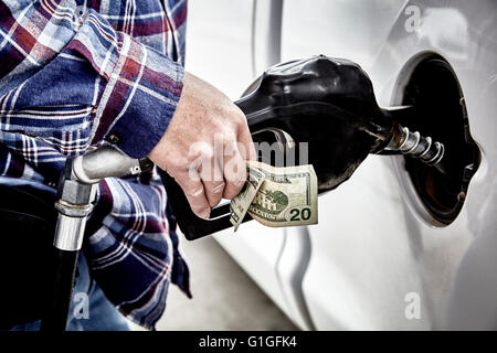 Hand des Mannes halten vierzig Dollar Bargeld und Gas Düse beim Pumpen Gas in geparkten Fahrzeug Stockfoto