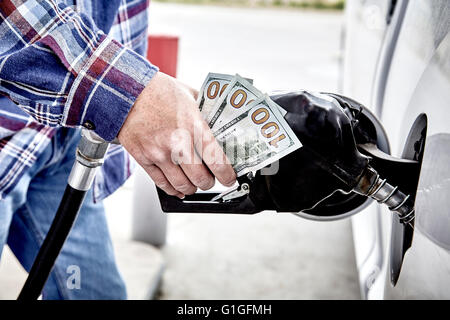 Hand des Mannes halten vierzig Dollar Bargeld und Gas Düse beim Pumpen Gas in geparkten Fahrzeug Stockfoto