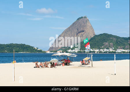 RIO DE JANEIRO - 5. April 2016: Beachgoers versammeln sich am Strand von Flamengo unter einen malerischen Blick auf den Zuckerhut. Stockfoto