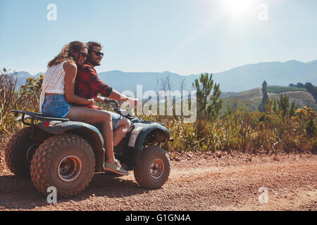 Glückliches junges Paar in der Natur auf einem Quad-Bike. Junger Mann und Frau genießen ein Quad-Bike fahren in Landschaft. Stockfoto