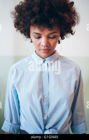 Vertikale Aufnahme des nachdenklichen jungen afrikanischen weibliches Modell mit dem lockigen Haar nach unten. Stilvolle Frau Hemd blickte. Stockfoto
