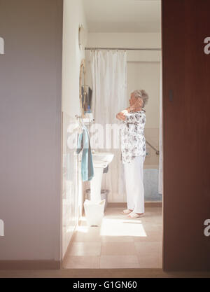 Voller Länge Innenaufnahme älteren Frau, die immer bereit auf die Kommode. Senioren weiblich immer im Badezimmer bereit. Stockfoto