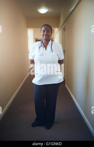 In voller Länge Portrait von Ärztin Krankenschwester stehen im Korridor des Pflegeheims. Fürsorgliche Krankenschwester Blick auf Kamera und smil Stockfoto